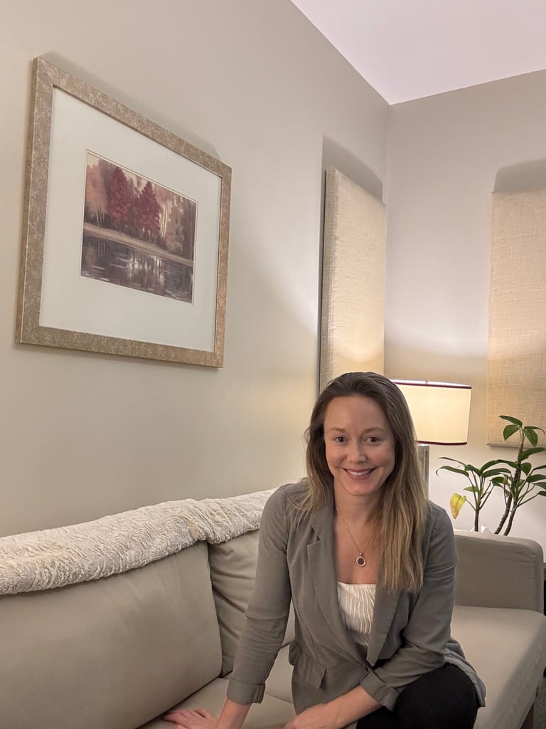 Woman sitting on a beige couch in a bright living room with framed art on the wall and a potted plant