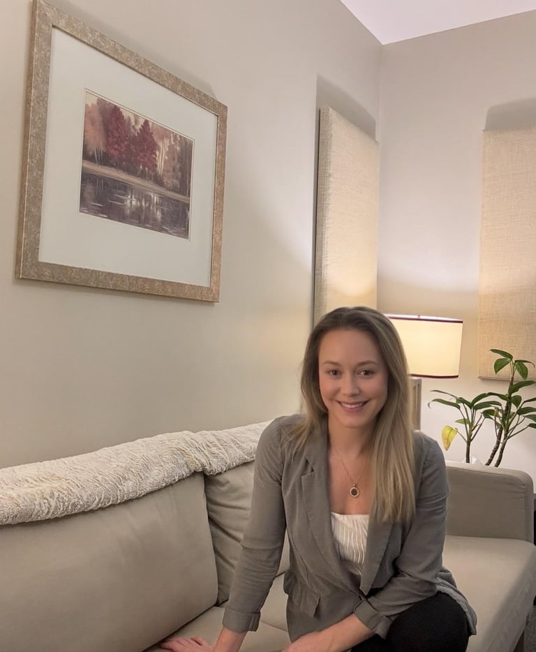 Woman sitting on beige sofa in modern living room with framed artwork and lamp visible in background